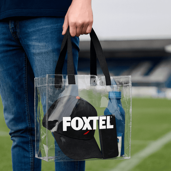 A clear stadium tote bag with black handles, a drink bottle, and a black cap inside. It features a logo.