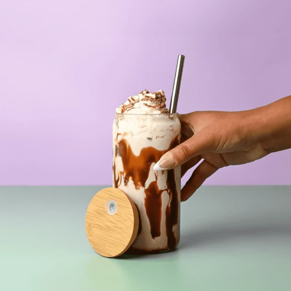 A drink bottle with a bamboo lid, featuring a creamy beverage topped with whipped cream, held in a hand.