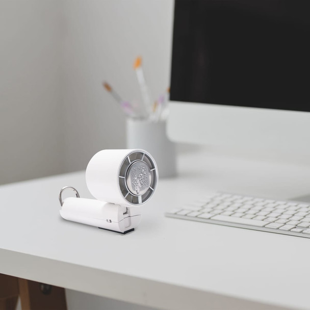 A compact white cooling fan on a desk next to a computer, featuring a circular fan design and a keychain attachment.