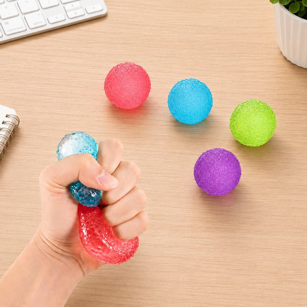 A hand squeezing a clear squishy stress relief mini ball, surrounded by coloured stress balls in red, blue, green, and purple.
