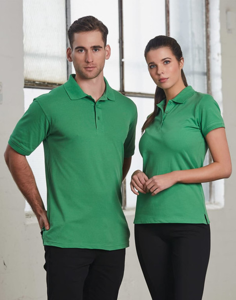 A green polo shirt featuring a logo, displayed on a male and female model against an industrial backdrop.
