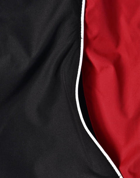 A close-up of a unisex jacket featuring black and red fabric with contrasting white piping.