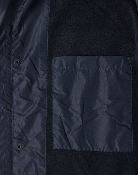 A navy unisex jacket featuring a pocket and snap buttons, made from a mix of materials. It has a logo.