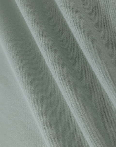 A close-up of light green cotton fabric with a smooth texture, showcasing fine weaves and folds.