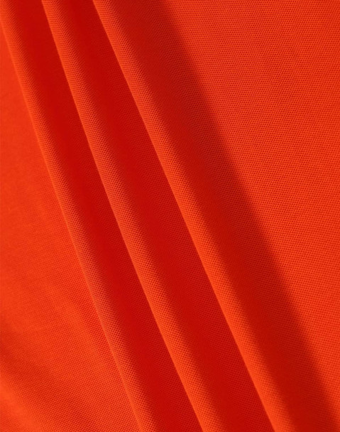 A close-up of orange fabric featuring a textured surface, ideal for polo shirts. The image includes a logo.