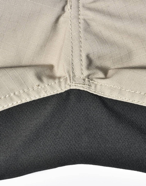 A close-up of Rip-Stop poly/cotton stretch work pants, featuring a beige upper section and a black lower section with stitching.