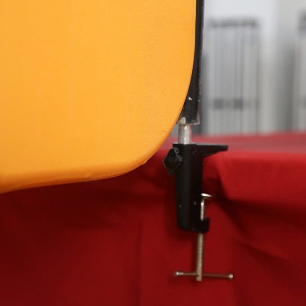 A bright orange table top banner with a black clamp securing it to a red tablecloth.