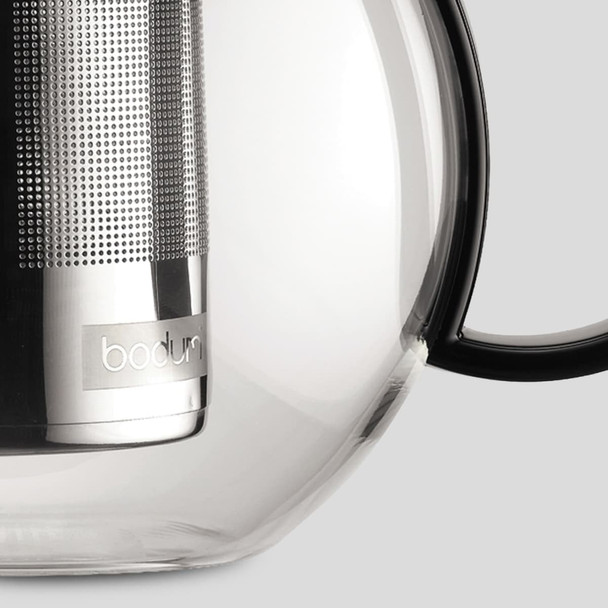 A glass tea press featuring a stainless steel infuser and a black handle, with a logo on the body.