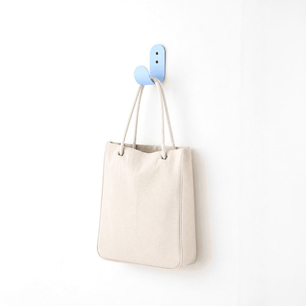 A cream-coloured tote bag hanging on a blue hook against a white wall. The bag has a simple design and a logo.