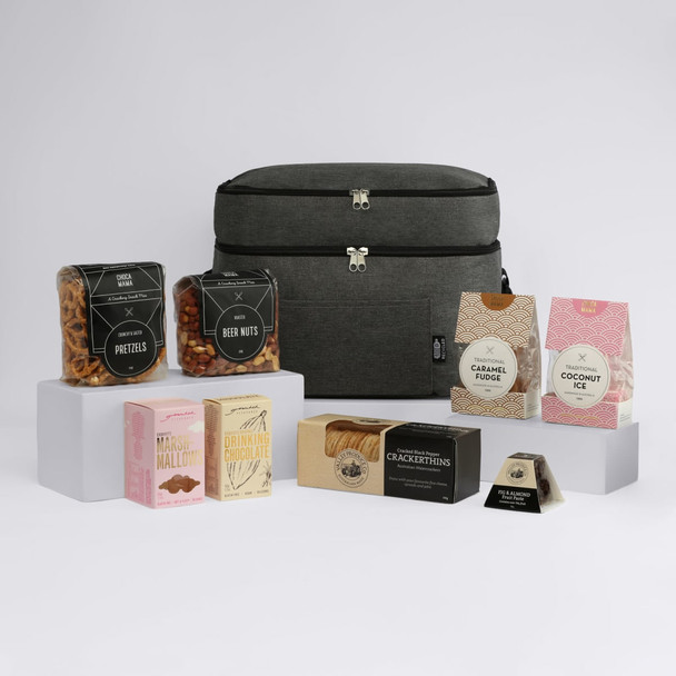 A grey promotional bag surrounded by various snacks, including pretzels, beer nuts, caramel fudge, and coconut ice.