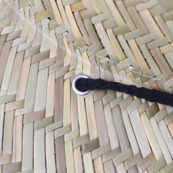 A close-up of a straw hat showcasing the woven texture and a black string threaded through a metal grommet.