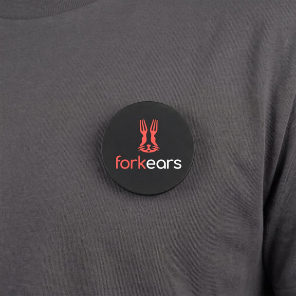 A round black magnetic badge featuring a logo and placed on a grey shirt.