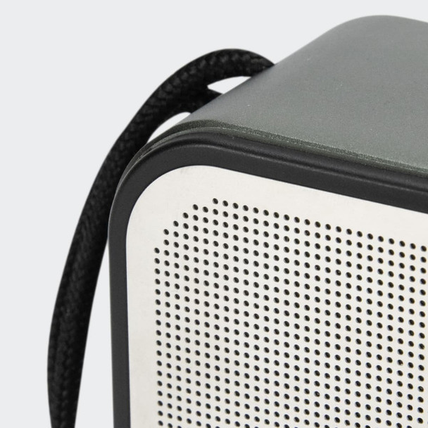 A grey and white portable speaker with a textured surface and a black strap attached.