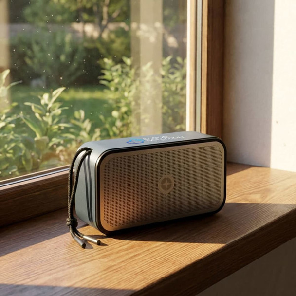 A grey Bluetooth speaker sits on a windowsill, showcasing a sleek design with a logo on its front.