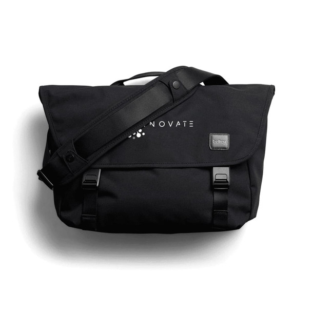 A black satchel bag with a shoulder strap and a logo, featuring front clasps and a flap cover.