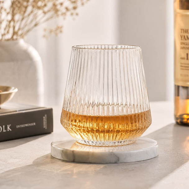 A drink bottle with a ribbed clear glass design sits on a marble coaster, featuring a golden liquid inside.