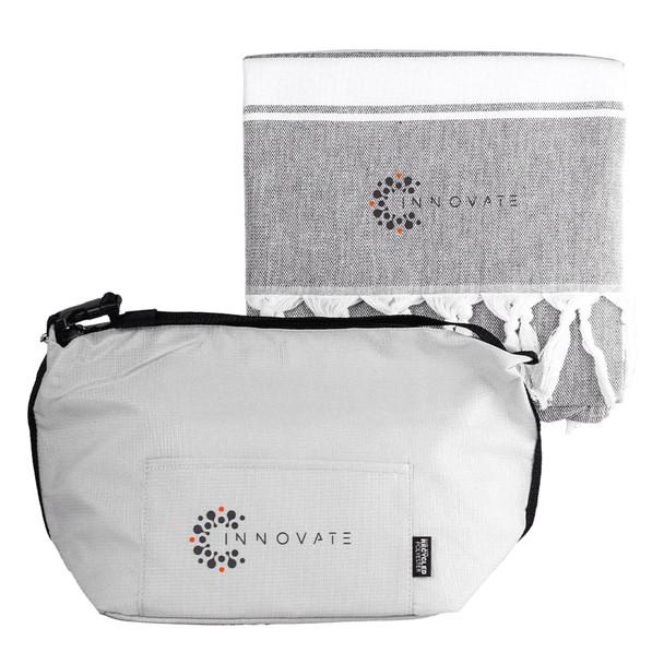 A grey cooler bag with a zipper and a matching grey towel featuring tassels. Both items have a logo.