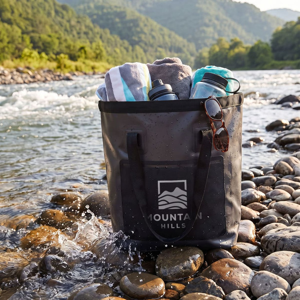A black bucket bag with towels and drink bottles sits on rocky riverbank, surrounded by a scenic landscape.