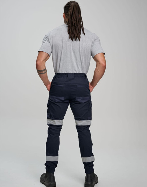 Cotton stretch drill cuffed work pants in navy with reflective tape, viewed from behind on a model.