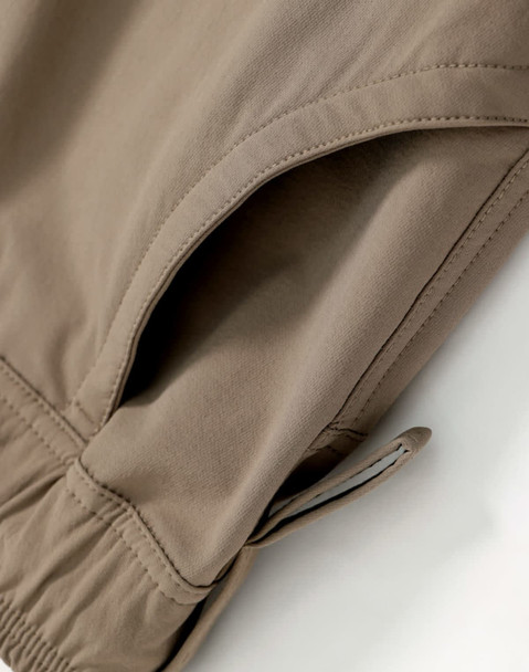A close-up of light brown flexi work pants, featuring an elastic cuff and a pocket detail. The product has a logo.