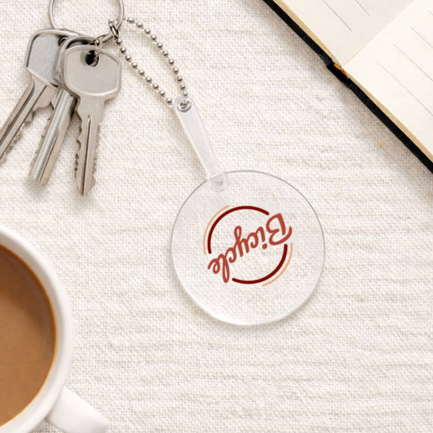 A clear PVC hand fan with a keychain, featuring a round shape, sits on a textured surface near a coffee cup and notebook.