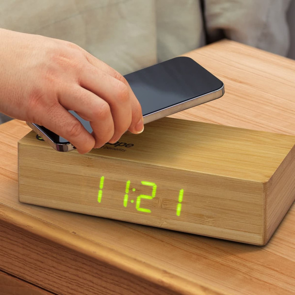 A bamboo wireless charging clock with a digital display. A smartphone is being placed on top for charging. A bamboo wireless charging clock with a digital display. A smartphone is being placed on top for charging.