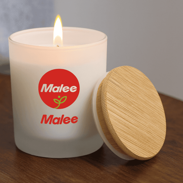 A small white candle with a wood lid, featuring a logo, and a lit flame on a wooden surface.