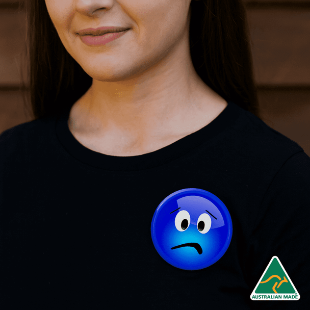 A blue button badge featuring a sad face, worn on a black shirt by a woman. The badge has a logo indicating it's Australian made. A blue button badge featuring a sad face, worn on a black shirt by a woman. The badge has a logo indicating it's Australian made.