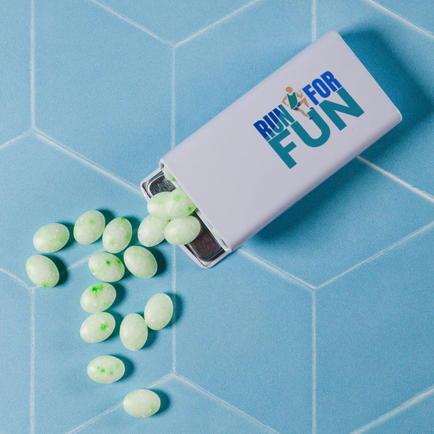 A flip top tin filled with light green spearmint mints is shown, with some mints scattered around.