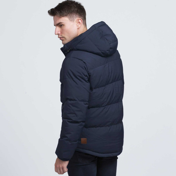 A navy puffer jacket with a hood, featuring a branded patch, displayed on a male model facing sideways.