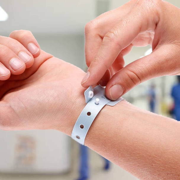 A light blue plastic wristband is being secured on a person's wrist, featuring multiple holes and a fastening.