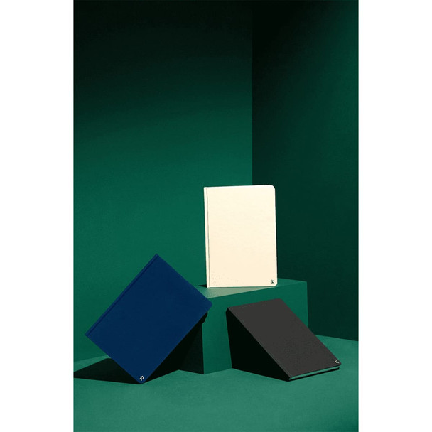 A collection of three Karst A5 stone paper hardcover notebooks in navy, cream, and black on a green backdrop.