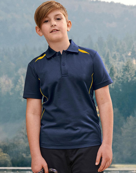 A boy stands outdoors wearing a navy polo shirt with yellow accents and a logo. The background features trees and hills.