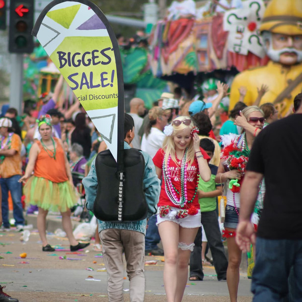 A Teardrop Backpack Flag features a vibrant design, prominently displaying a logo, in a bustling festive environment.