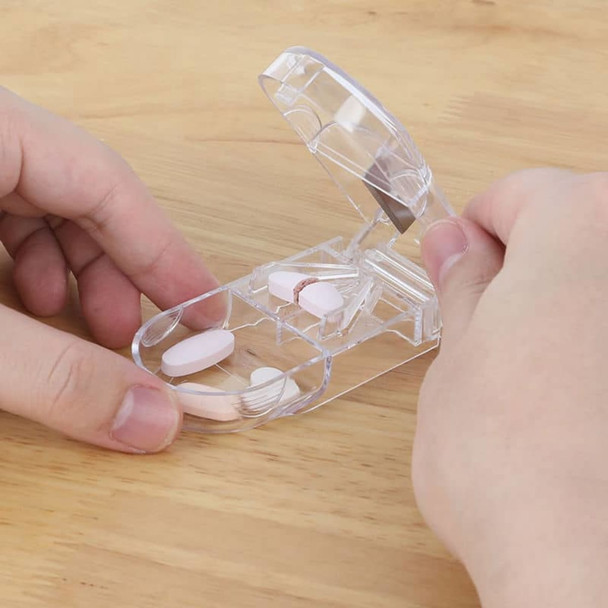 A clear plastic pill box with a cutter, containing several pink and white pills, resting on a wooden surface.