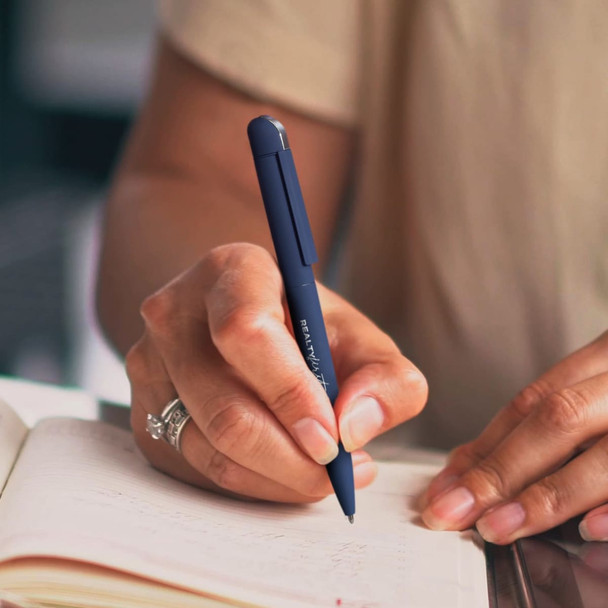 A hand holding a navy blue metal pen, writing in a notebook. The pen has a sleek design and features a logo.