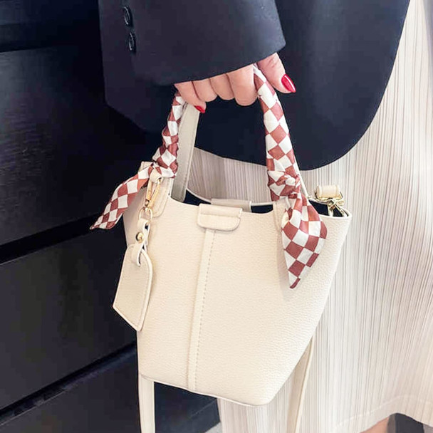 A cream handbag with a checked silk chiffon scarf tied to the handle, held by a hand with red nails.