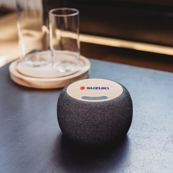 A wireless speaker with a bamboo top and a dark fabric body, featuring a logo on the top.
