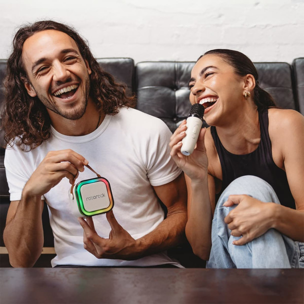 A portable karaoke machine in rainbow colours, held by a smiling man, while a woman sings with a microphone. A portable karaoke machine in rainbow colours, held by a smiling man, while a woman sings with a microphone.