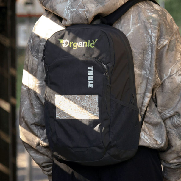 A black Thule Achiever 15 laptop backpack with a logo, worn by a person in a camouflage hoodie.