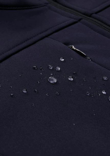 A dark navy softshell jacket with water droplets beading on the fabric, featuring a zippered pocket.