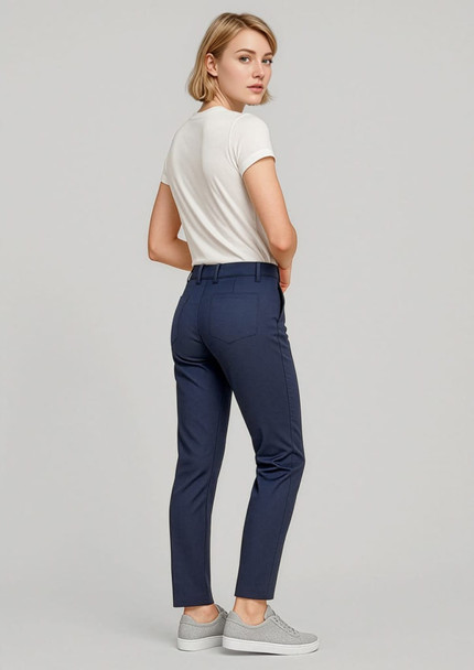 A woman stands wearing navy slim leg stretch chino pants and a white top, paired with grey sneakers.