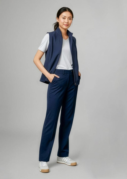 A woman in navy slacks stands confidently, wearing a white t-shirt and a matching vest, with hands in pockets.