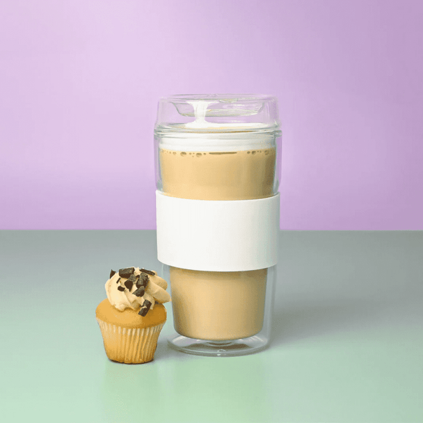A reusable coffee cup in clear and white, featuring a logo, beside a cupcake on a pastel background.