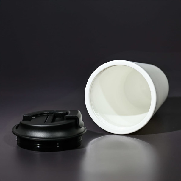 A white coffee mug made from recycled materials, featuring a black lid, displayed on a dark background.