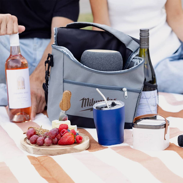 A grey cooler bag with various beverages, fruits, and snacks arranged on a picnic blanket.