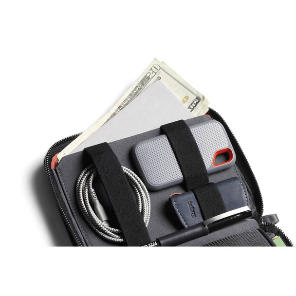A grey toiletry bag with compartments holding cash, a phone case, a cable, and a pen against a dark background.
