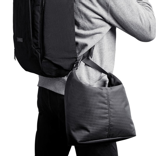 A cooler bag in a grid pattern, featuring a shoulder strap, being carried on the side of a person with a backpack.