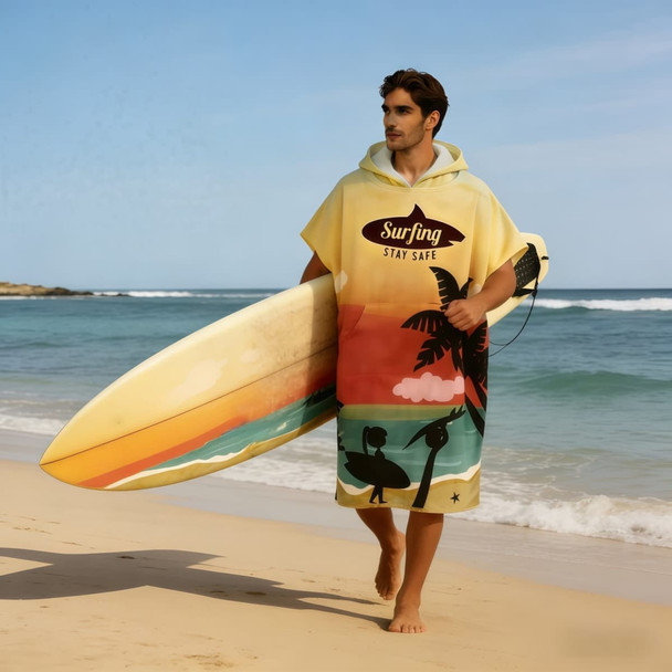 A man in a yellow cotton surf poncho with a palm tree design, holding a surfboard on the beach.