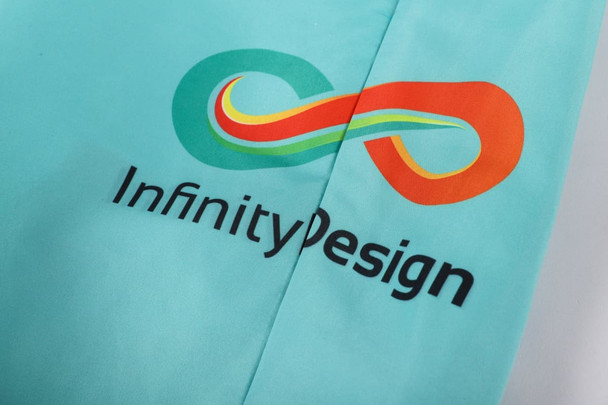 A pair of turquoise beach shorts featuring a multicoloured logo and the text "InfinityDesign."
